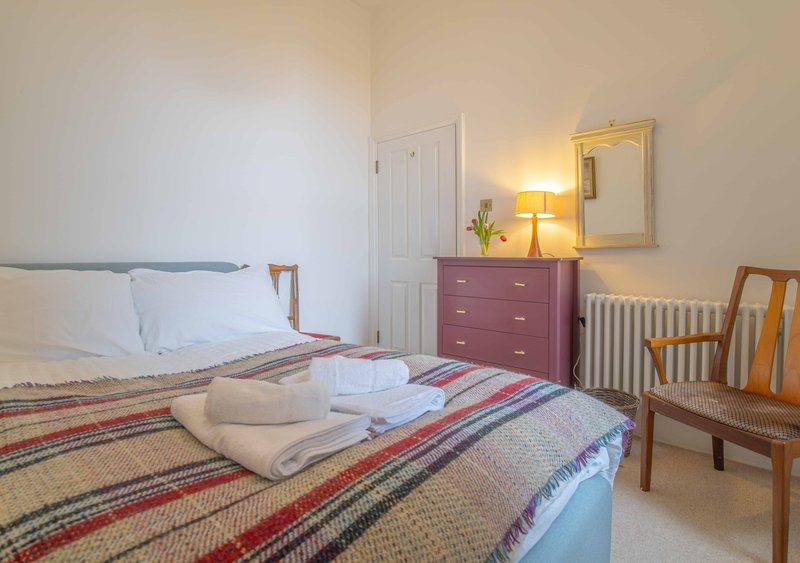 Bedroom with double bed, wooden chair, burgundy dresser, mirror, and table lamp