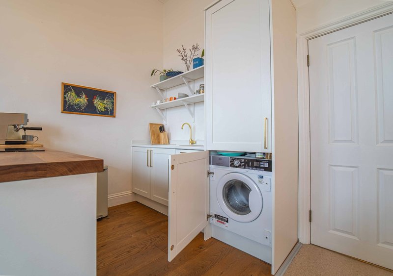 Compact kitchen with washing machine, white cabinetry, wooden countertop and shelving