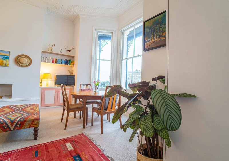 Bright studio apartment with dining table, shelving, potted plant, and large windows