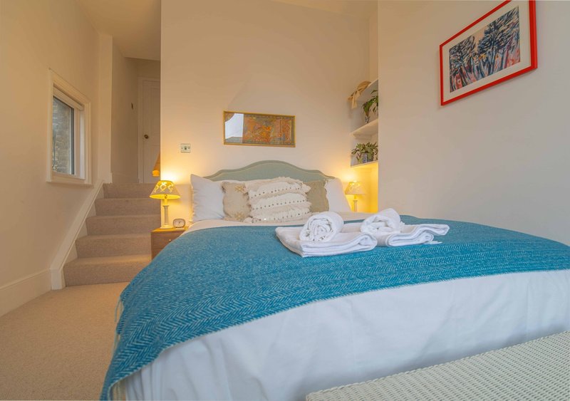 Bedroom with double bed, blue throw, white pillows, bedside lamps and stairs visible