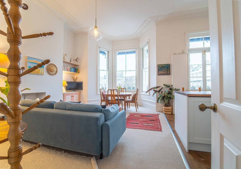 Bright living room with blue sofa, wooden shelving, dining area and large windows overlooking landscape