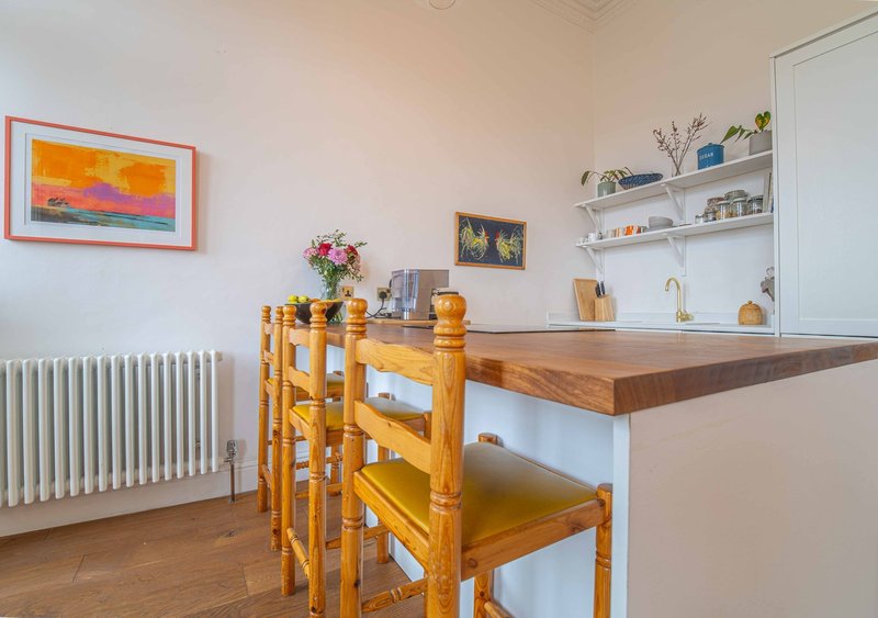 Modern kitchen with wooden counter, white shelving, radiator, and dining chairs