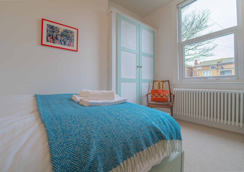 Bright bedroom with single bed, blue throw blanket, large window and framed wall art