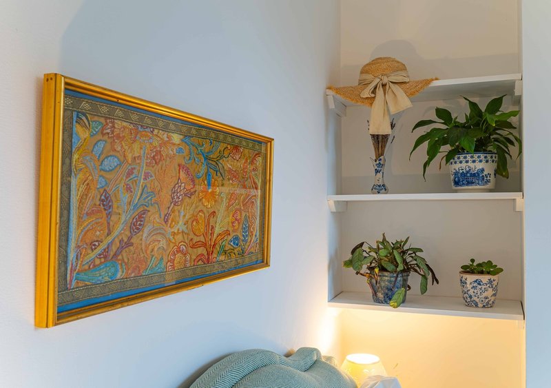Bright bedroom corner with framed artwork, floating shelves displaying potted plants and decorative items