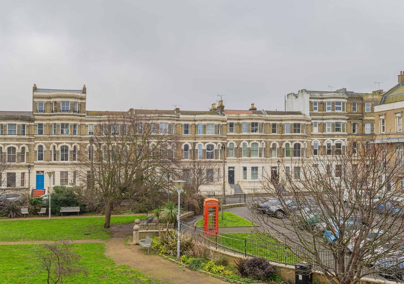 Victorian terrace buildings with green lawn, bare trees and red telephone box in foreground