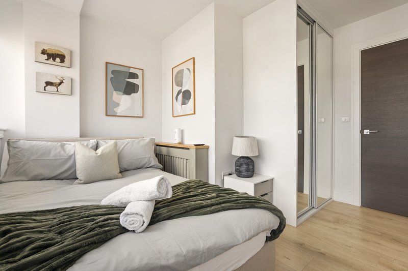 Modern bedroom with double bed, green throw blanket, framed wall art, and ensuite door