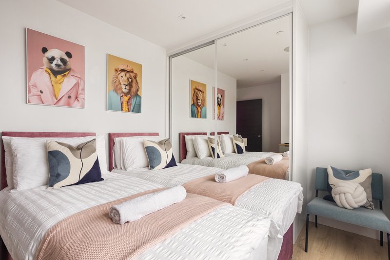 Modern bedroom with two beds, pink headboards, colorful animal artwork on walls, and large mirror