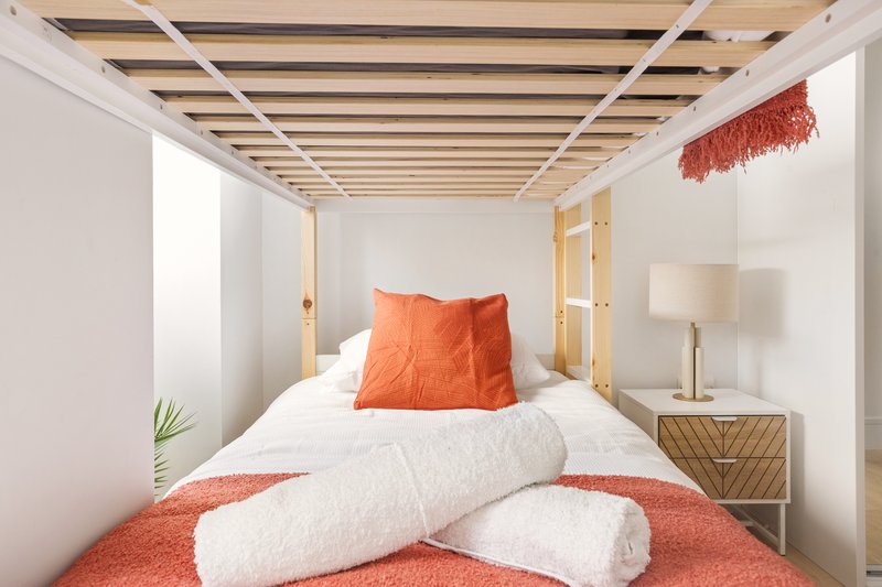 Modern bedroom with wooden bed frame, white bedding, orange pillows and throws