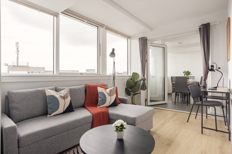 Modern open-plan living room with grey sofa, round coffee table, large windows and work area