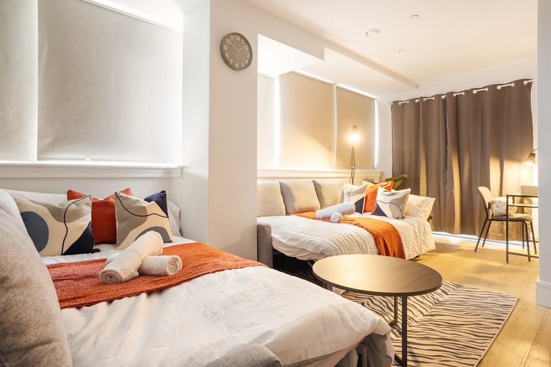 Modern studio apartment with two beds, orange accents, wooden flooring and contemporary furnishings
