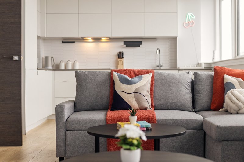 Modern open-plan living room with gray sectional sofa, kitchen area with white cabinetry, and black coffee table
