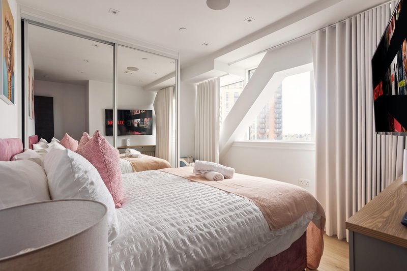 Modern bedroom with double bed, pink pillows, large mirror wardrobe and city views