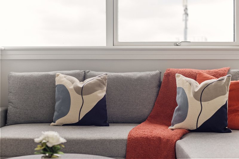 Modern gray sofa with decorative pillows and red throw blanket near large window