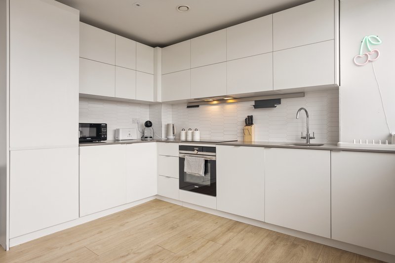 Modern white kitchen with built-in oven, wooden floor and countertop appliances