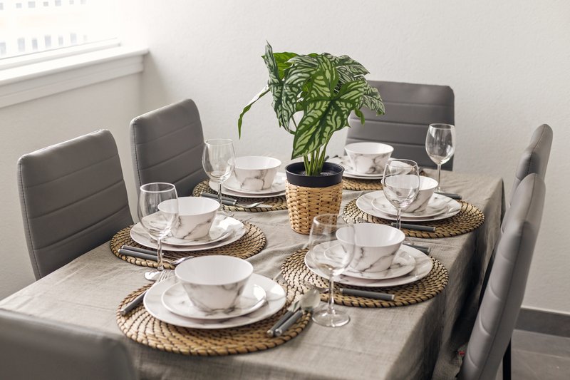 Dining table set for four with white plates, glasses, and potted plant centerpiece