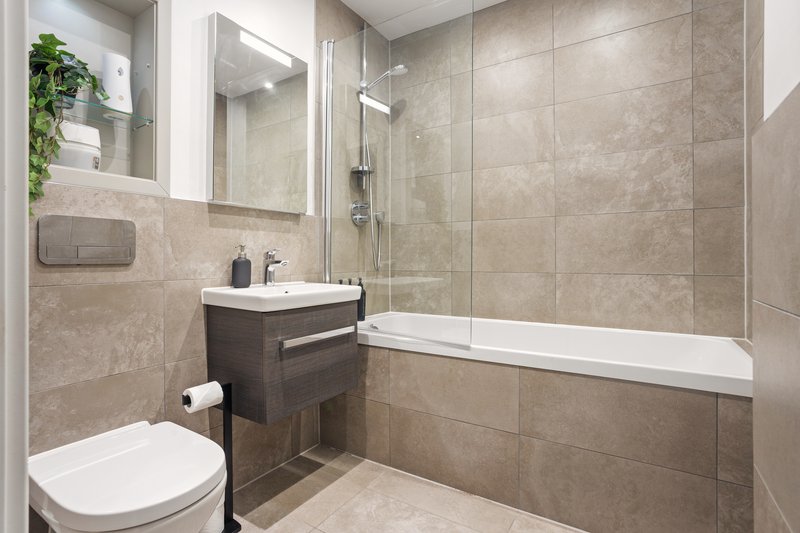 Modern bathroom with toilet, vanity sink, mirror, shower enclosure and beige tile walls