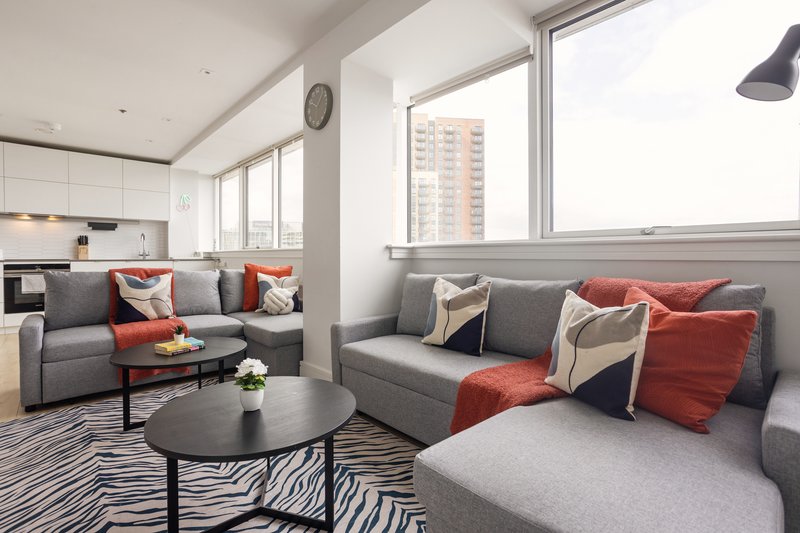 Open-plan living room with grey sofas, red cushions, black coffee table and kitchen area