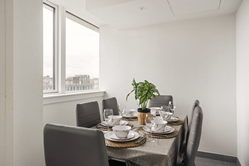 Dining area with table, grey chairs, place settings, plant and city view window
