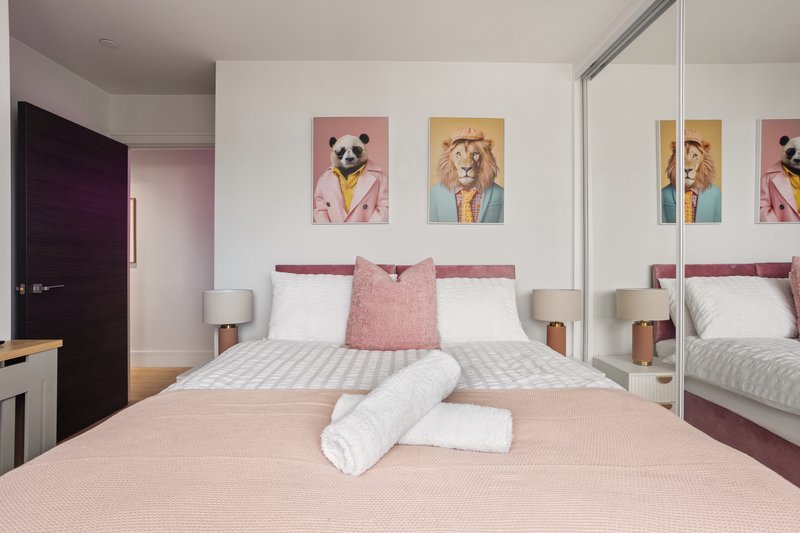 Modern bedroom with pink bedding, white pillows, framed animal artwork, and mirrored wardrobe