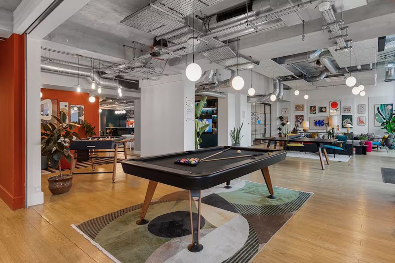 Modern open-plan office or communal space with pool table, wooden flooring, and pendant lighting