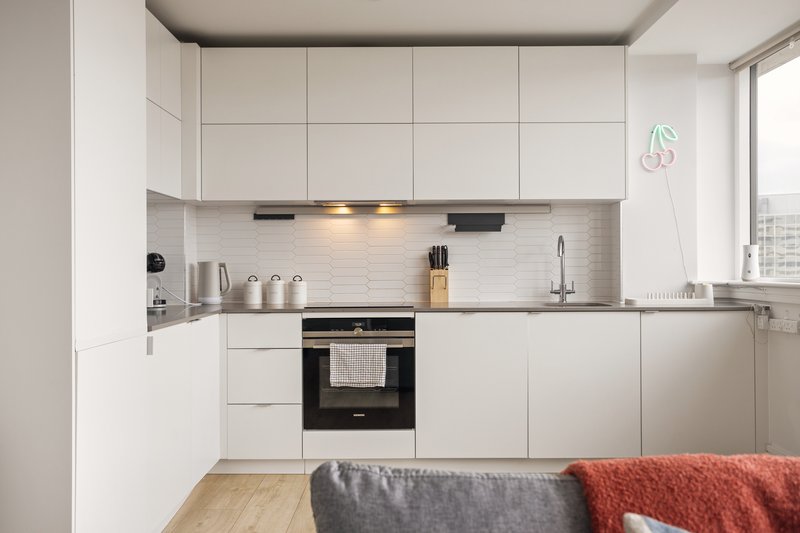 Modern white kitchen with black oven, stainless steel appliances and wooden flooring