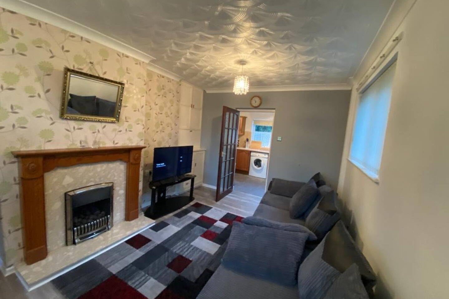 Living room with fireplace, sofa, TV, patterned wallpaper and wooden mantelpiece