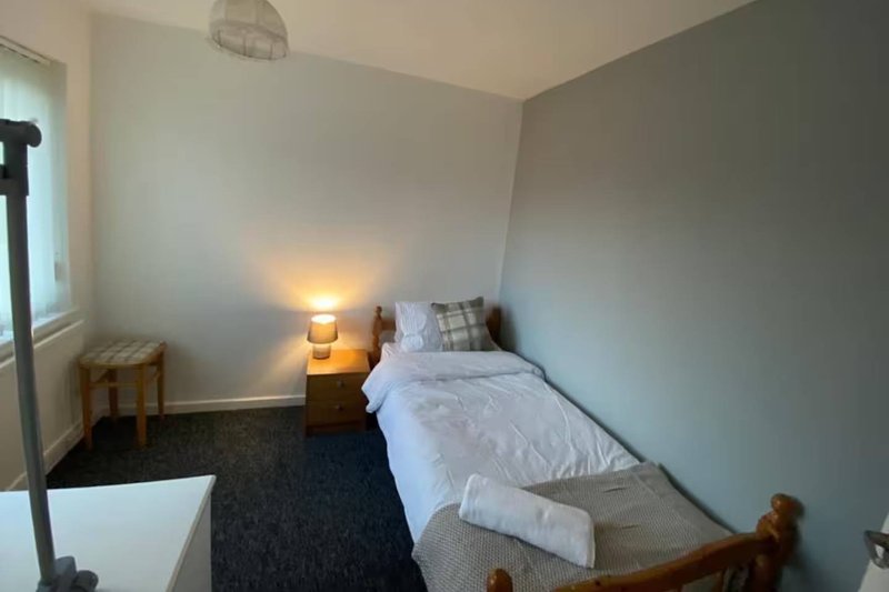 Small bedroom with single bed, bedside lamp, wooden stool and window