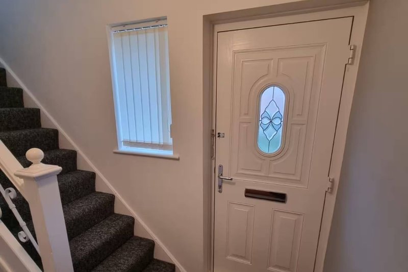 Hallway with staircase, front door with glass panel, and vertical blinds on window