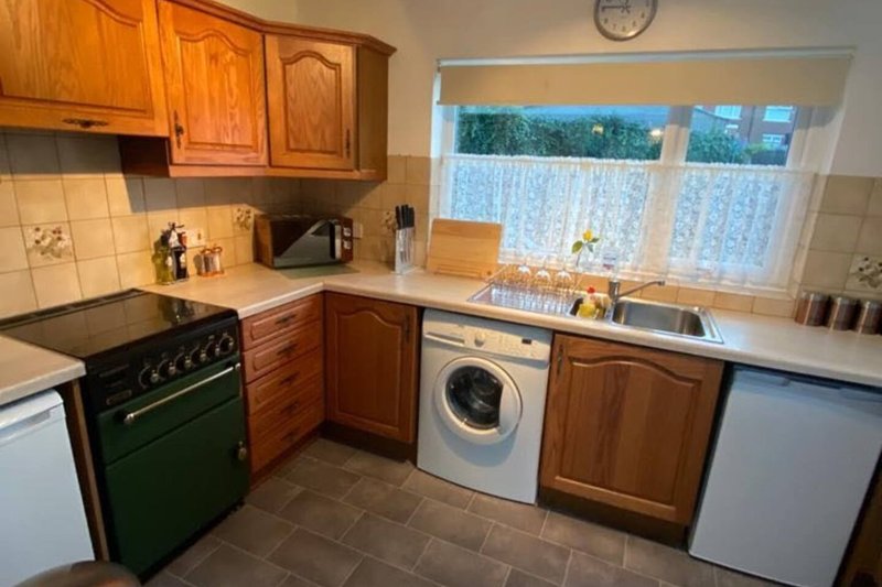 Kitchen with wooden cabinets, green oven, washing machine, and window with countryside view