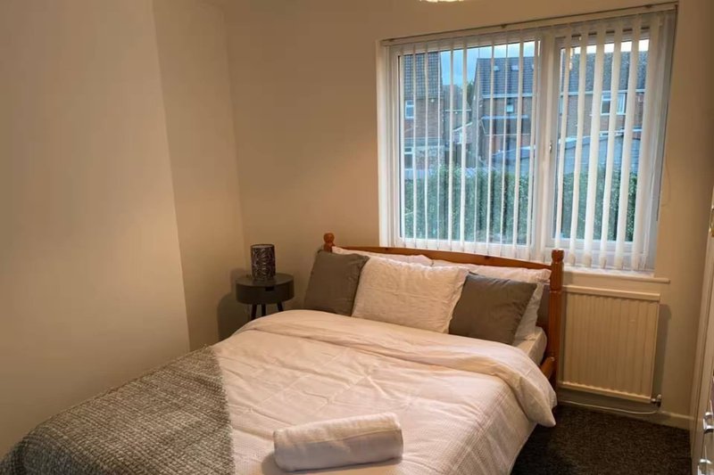 Bedroom with double bed, wooden headboard, beige bedding, and vertical blind windows