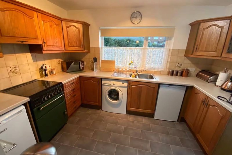 Kitchen with wooden cabinets, black range cooker, washing machine, and window overlooking garden