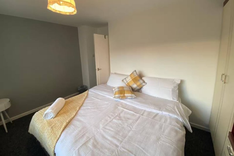 Bedroom with double bed, white bedding, yellow throw, and pillows