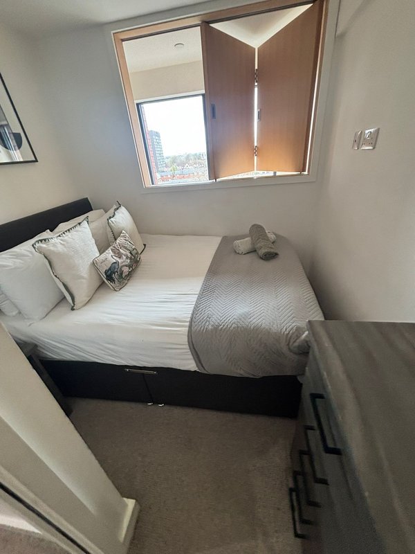 Compact bedroom with single bed, pillows, window with city view, and neutral decor.