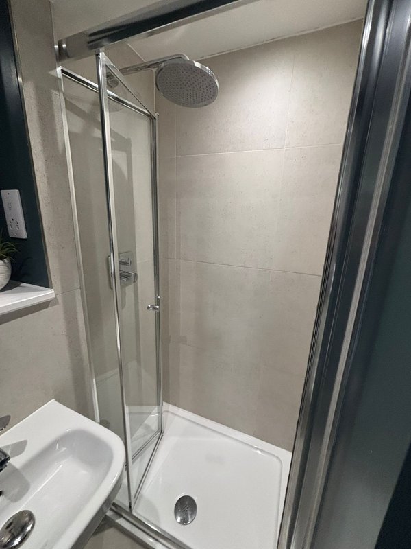 Modern bathroom with enclosed shower cubicle, white basin and tiled walls