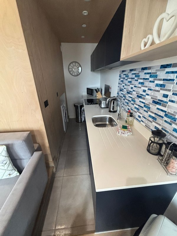 Narrow modern kitchen with blue tile backsplash, white countertop, sink and appliances