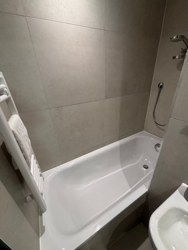 Modern bathroom with white bathtub, grey tile walls, shower fixtures and towel rack