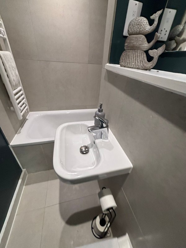 Compact bathroom with white sink, chrome faucet, toilet, and wall-mounted shelf with decorative items.