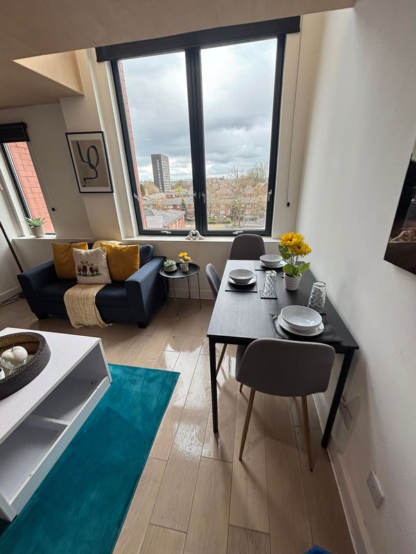 Modern open-plan living area with dining table, blue armchair, and city view from large windows