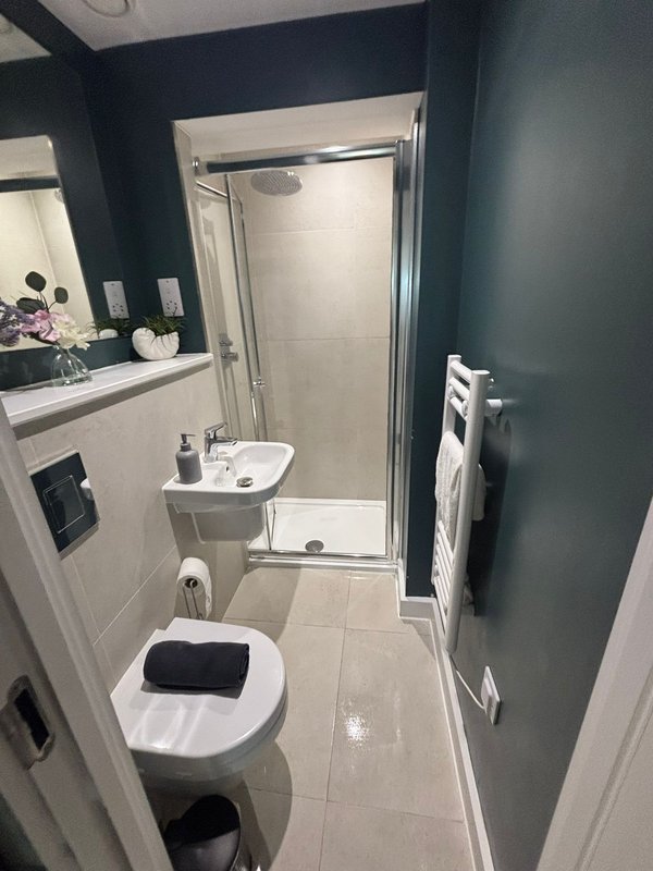 Modern bathroom with toilet, sink, mirror, and shower enclosure with dark accent wall