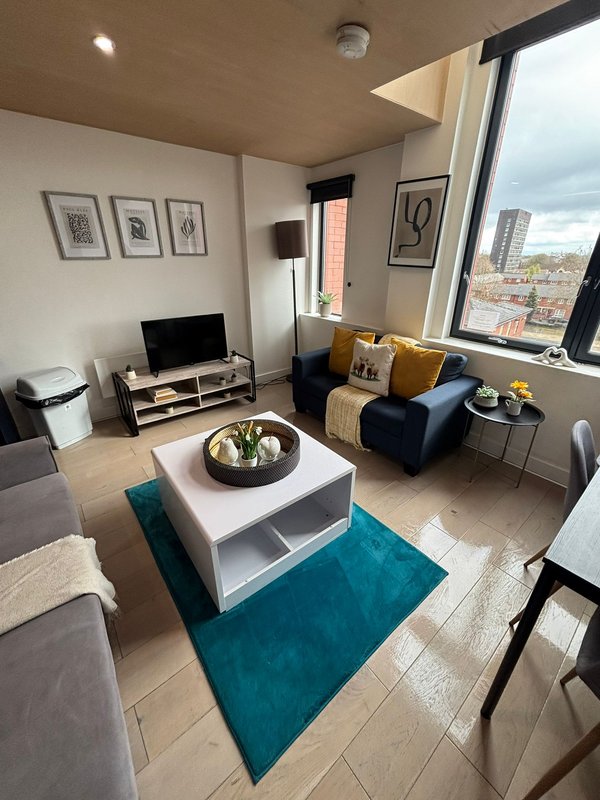 Modern living room with sofa, TV stand, white coffee table, and city views through floor-to-ceiling windows