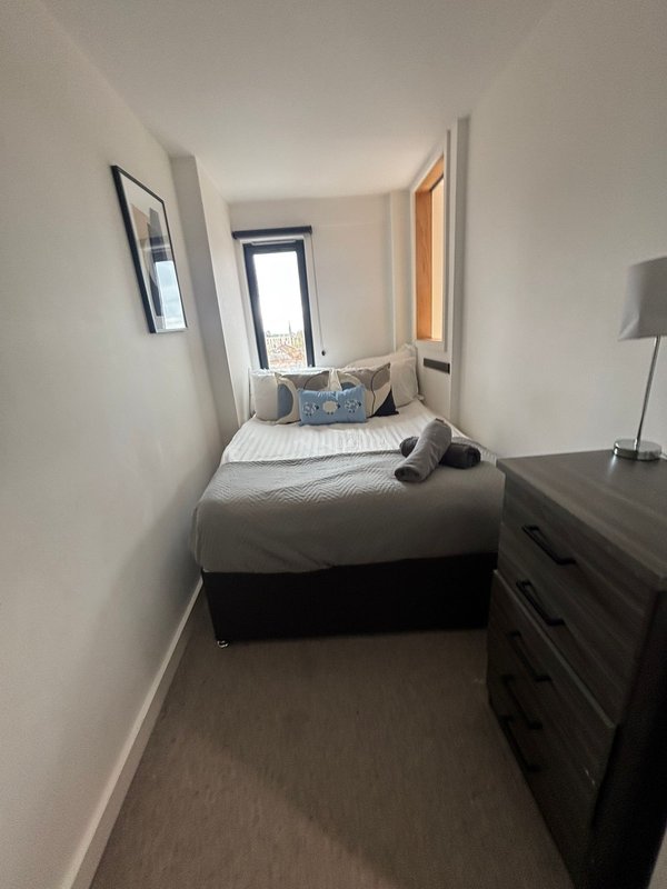 Narrow bedroom with single bed, dark wooden dresser, bedside lamp, and window.