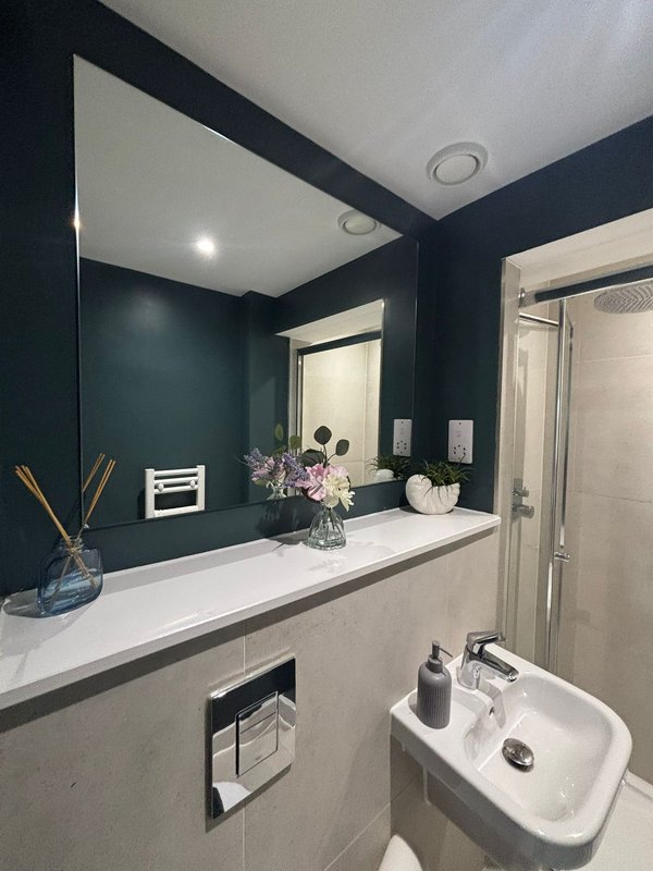 Modern bathroom with dark teal walls, white vanity, large mirror and fresh flowers in vase