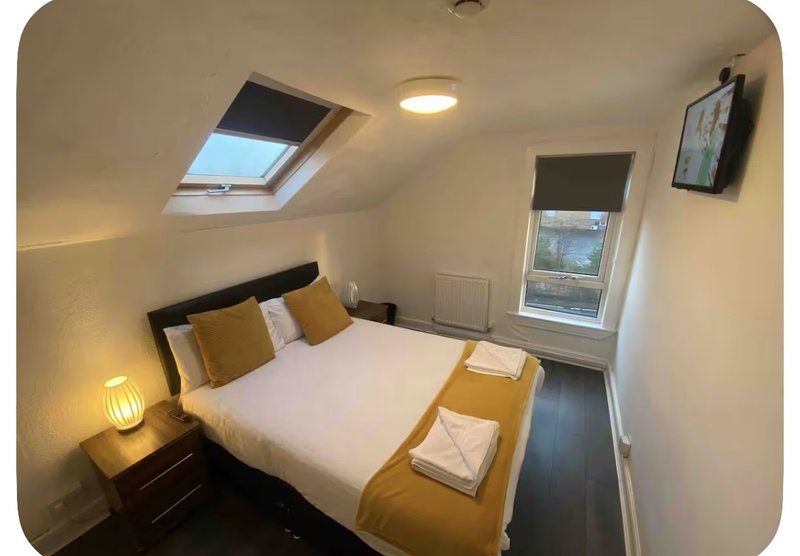 Bright attic bedroom with double bed, skylight window, bedside lamp and wall-mounted TV