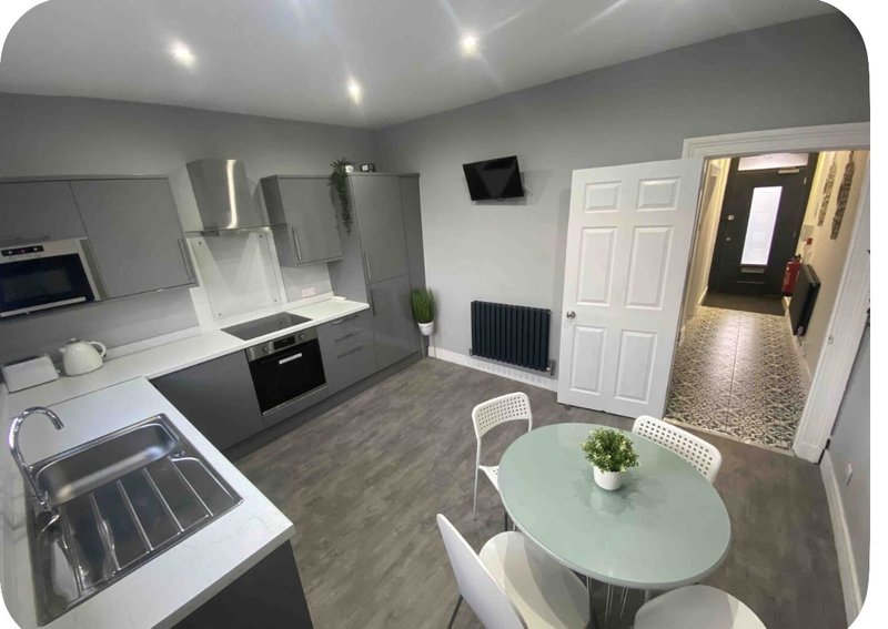Modern kitchen and dining area with grey cabinetry, stainless steel appliances, round table and hallway entrance