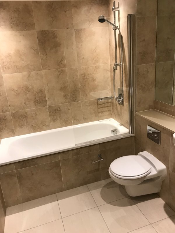 Modern bathroom with bathtub, glass shower enclosure, toilet, and neutral tile walls