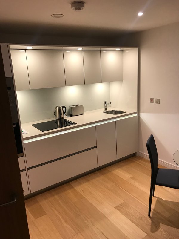 Modern kitchenette with white cabinetry, black countertop, sink, and wooden flooring