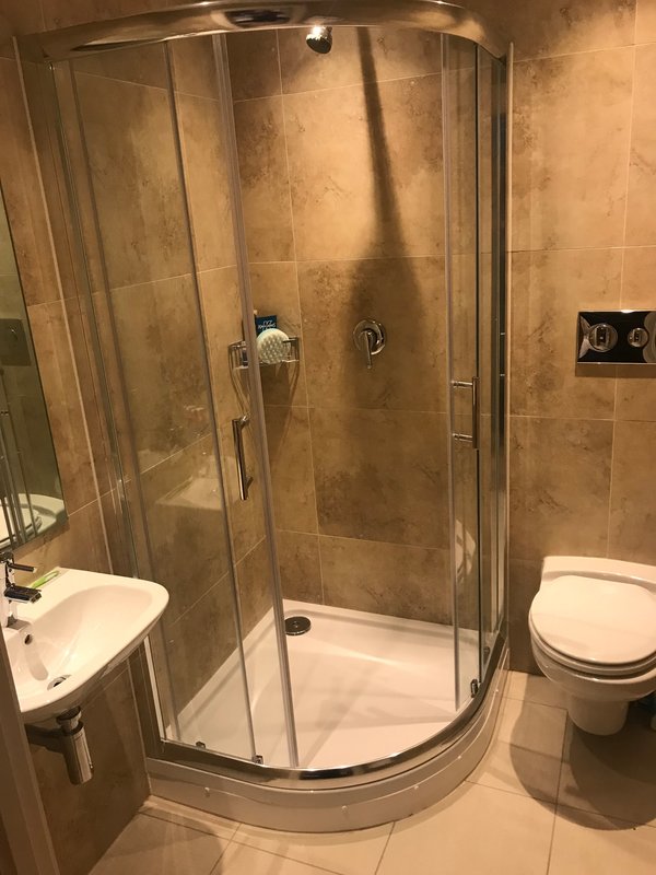 Bathroom with curved glass shower enclosure, white sink, toilet, and beige tile walls