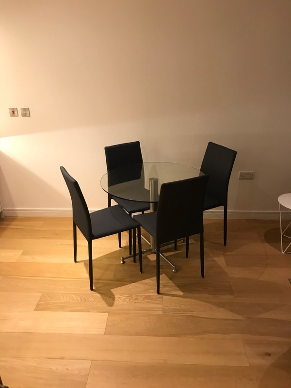 Dining area with round glass table, three black chairs, wooden flooring