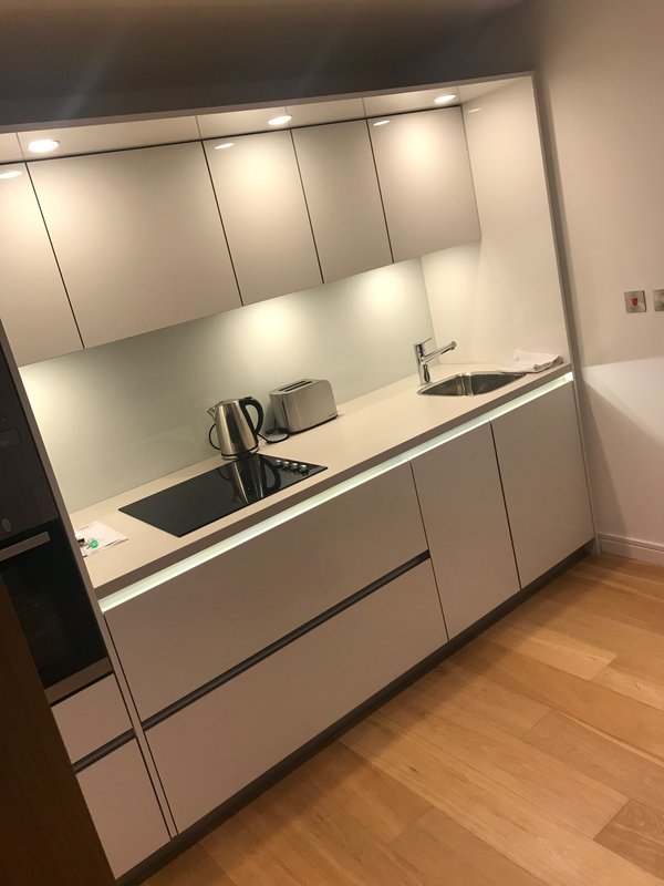 Modern kitchenette with white cabinetry, integrated sink, kettle, and wooden flooring