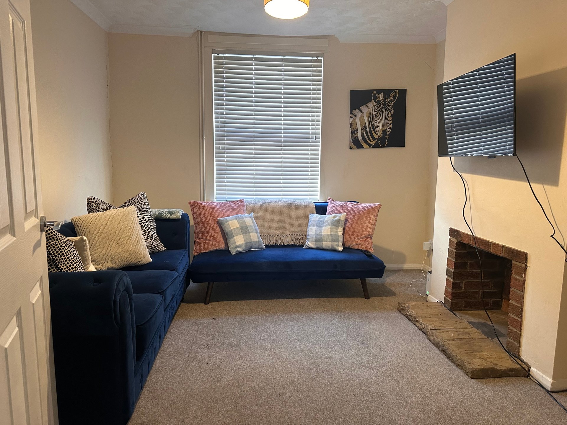 Living room with blue sofa, decorative pillows, windows with blinds, and fireplace